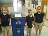 Three children pose next to recycling container