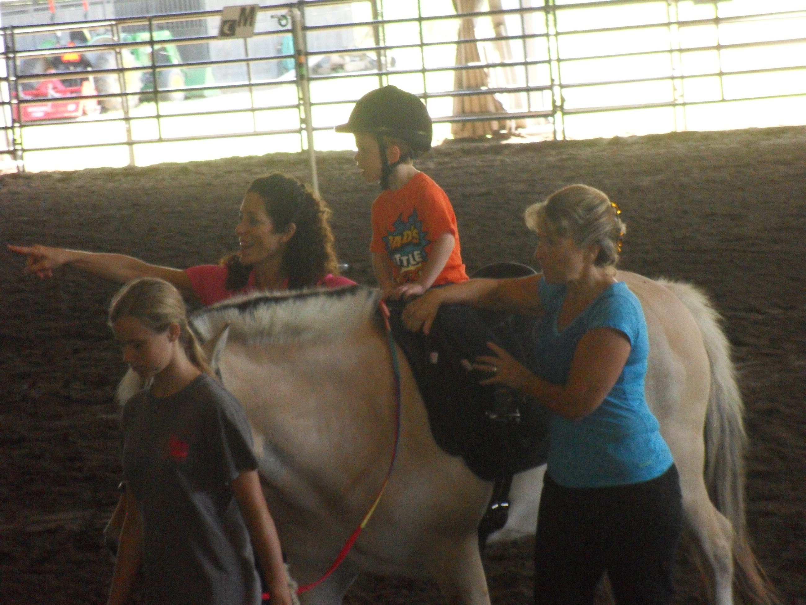 Little Kid riding a horse with women assisting it